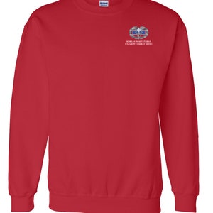 May include: Red sweatshirt with a white embroidered patch on the left chest. The patch features a silver Korean War Veteran badge with the text "KOREAN WAR VETERAN U.S. ARMY COMBAT MEDIC".