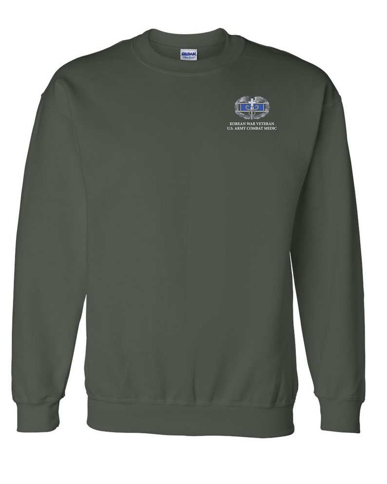 May include: A dark green sweatshirt with a small embroidered patch on the left chest. The patch features a silver and blue Korean War Veteran U.S. Army Combat Medic badge.