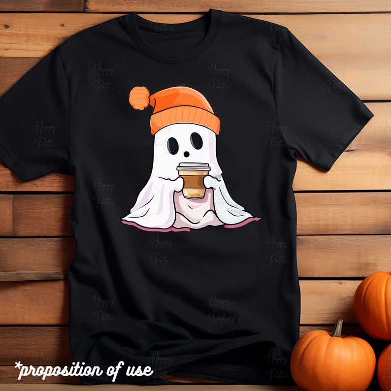 May include: Black t-shirt with a cartoon ghost wearing an orange beanie and holding a cup of coffee. The ghost is sitting on a pink blanket.