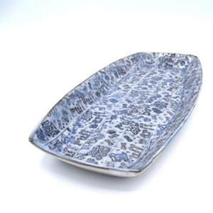 May include: A rectangular ceramic serving tray with a blue and white floral pattern. The tray has a slightly raised edge and a textured surface. The design includes the word "WOW" in the pattern. The tray is on a white background.