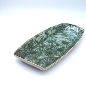 May include: Rectangular ceramic serving dish with a floral pattern in shades of teal and green. The dish has a slightly raised edge and a glossy finish. The floral design covers the entire surface of the dish.