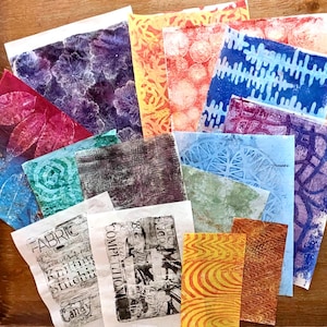May include: A collection of rectangular paper sheets featuring various monoprint designs in colours including purple, red, blue, orange, green, and black. Some sheets display leaf imprints, geometric patterns, and text reading FABRIC and COMPETITION.