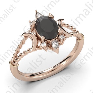 Puede incluir: Un anillo de oro rosa con una piedra ovalada negra rodeada de piedras blancas m&aacute;s peque&ntilde;as. El anillo presenta un dise&ntilde;o de cuerda trenzada y dos formas de luna creciente.