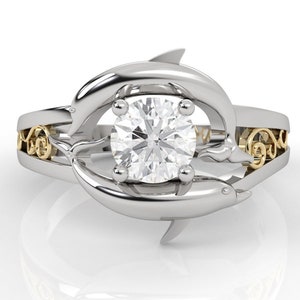 May include: A silver ring with two dolphins intertwined around a large, clear, round diamond. The dolphins are accented with yellow gold.
