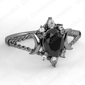 Puede incluir: Anillo negro con una piedra ovalada negra rodeada de piedras blancas m&aacute;s peque&ntilde;as. La banda del anillo es un dise&ntilde;o de cuerda trenzada con dos lunas crecientes a cada lado de la piedra preciosa.