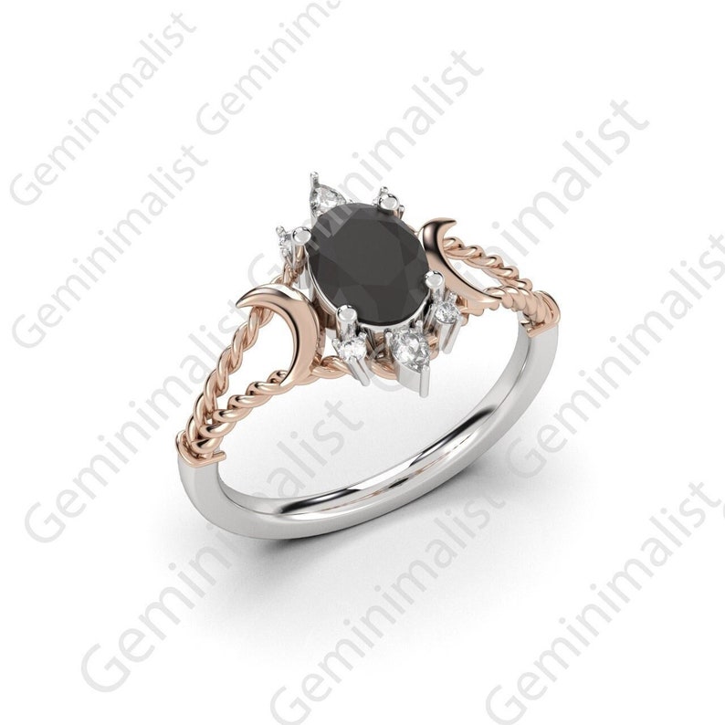 Puede incluir: Un anillo de plata y oro rosa con una piedra ovalada negra rodeada de piedras blancas m&aacute;s peque&ntilde;as. El anillo presenta dos dise&ntilde;os de luna creciente a cada lado de la piedra.