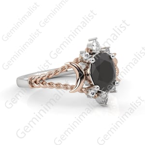 Puede incluir: Un anillo de plata y oro rosa con una piedra preciosa negra rodeada de piedras blancas m&aacute;s peque&ntilde;as. El anillo presenta una banda retorcida y un dise&ntilde;o de luna creciente.