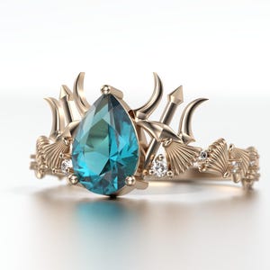 May include: A gold ring featuring a pear-shaped, teal gemstone. The ring has a detailed design with trident and seashell motifs, and small accent diamonds. The ring's design is reminiscent of a crown.
