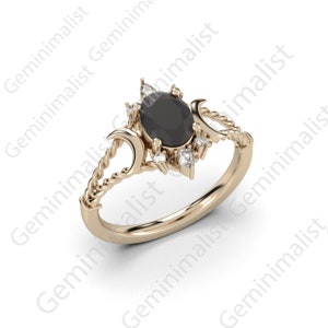 Puede incluir: Un anillo de oro con una piedra ovalada negra rodeada de piedras blancas m&aacute;s peque&ntilde;as. El anillo presenta un dise&ntilde;o de cuerda trenzada y dos formas de luna creciente.