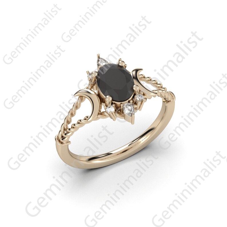 Puede incluir: Un anillo de oro con una piedra ovalada negra rodeada de piedras blancas m&aacute;s peque&ntilde;as. El anillo presenta un dise&ntilde;o de cuerda trenzada y dos formas de luna creciente.
