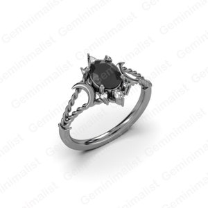 Puede incluir: Un anillo negro con una piedra ovalada negra rodeada de piedras blancas m&aacute;s peque&ntilde;as. La banda del anillo est&aacute; retorcida y presenta dos dise&ntilde;os de luna creciente.