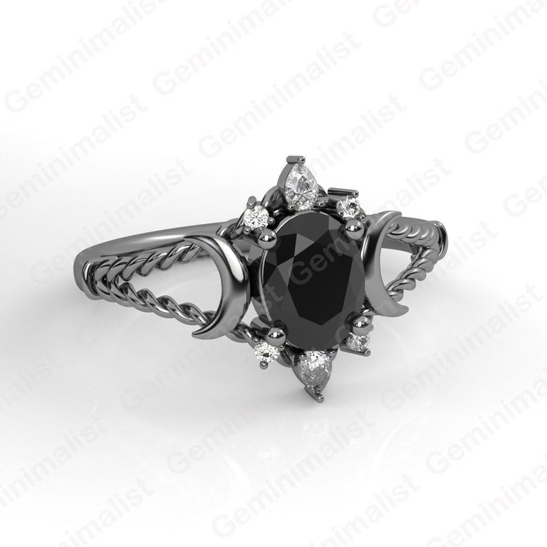 Puede incluir: Anillo negro con una piedra ovalada negra rodeada de piedras blancas m&aacute;s peque&ntilde;as. La banda del anillo es un dise&ntilde;o de cuerda trenzada con dos lunas crecientes a cada lado de la piedra preciosa.