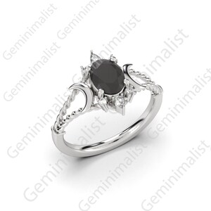 Puede incluir: Un anillo de plata con una piedra ovalada negra rodeada de piedras blancas m&aacute;s peque&ntilde;as. El anillo presenta un dise&ntilde;o de cuerda trenzada y dos formas de luna creciente.