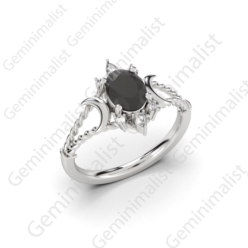 Puede incluir: Un anillo de plata con una piedra ovalada negra rodeada de piedras blancas m&aacute;s peque&ntilde;as. El anillo presenta un dise&ntilde;o de cuerda trenzada y dos formas de luna creciente.
