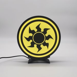 May include: A black and yellow round lamp with a stylized sun design. The lamp has a black base.