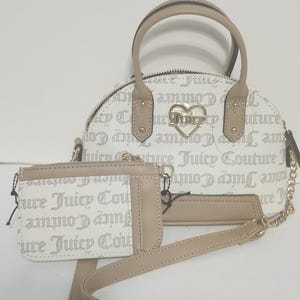 May include: A white and tan handbag set featuring a dome-shaped purse with a top handle and a small wallet. The set is adorned with the text "Juicy Couture" and a heart-shaped logo. The purse has a gold chain strap.