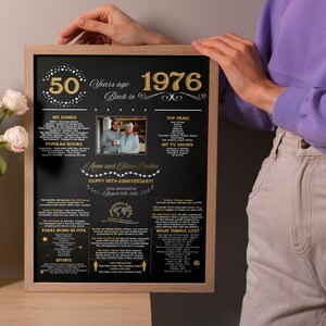 May include: A framed black poster with gold text and graphics commemorating a 50th anniversary from 1976. It features a central photograph of a couple, lists of hit songs, films, TV shows, popular books, and historical facts from that year.