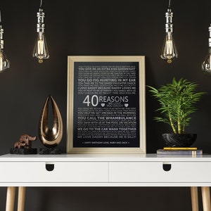 May include: A black and white printable poster with a white background and black text. The text lists 40 reasons to love a dad. The poster is framed in a light wood frame and is sitting on a white desk with a gold metal sculpture and a potted plant.