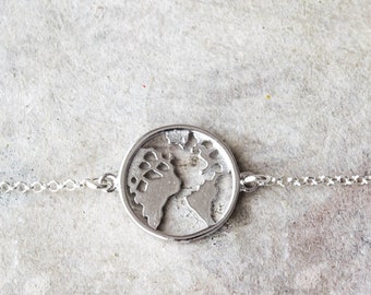 May include: A silver chain bracelet with a round pendant featuring a cut-out design of the world.