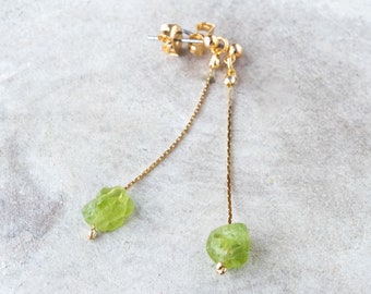 Könnte beinhalten: Ein Paar goldene Ohrringe mit grünen Edelstein-Tropfen. Die Ohrringe sind aus einer zarten Kette gefertigt und haben am Ende jeder Kette einen kleinen, facettierten Edelstein.