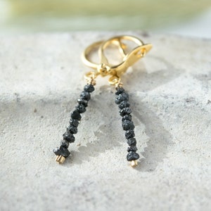 Peut inclure: Une paire de boucles d'oreilles en or avec des accents de diamants noirs. Les boucles d'oreilles sont de style pendantes et présentent une rangée de diamants noirs.