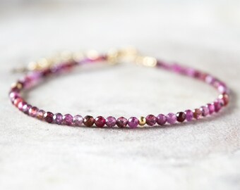 May include: A delicate bracelet made with small pink and red gemstone beads and gold accents.