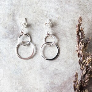 May include: A pair of silver dangle earrings with two interlocking circles. The earrings have a simple, modern design.