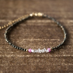 May include: A delicate black beaded bracelet with a small row of clear and pink gemstones.