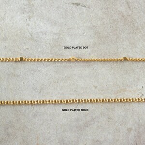 Pode incluir: Duas correntes banhadas a ouro, uma com um padr&atilde;o de pontos e a outra com um padr&atilde;o rolo. O texto "GOLD PLATED DOT" e "GOLD PLATED ROLLO" est&aacute; escrito abaixo de cada corrente.