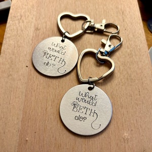 May include: Two silver keychains with heart-shaped charms. Each keychain has a round tag with the text "What would Beth do?" engraved on it.