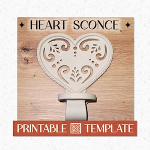 May include: A white heart-shaped wall sconce with intricate cut-out scrollwork patterns. The text HEART SCONCE is displayed at the top, and the text PRINTABLE TEMPLATE is at the bottom on a red rectangular banner with a small floral icon.