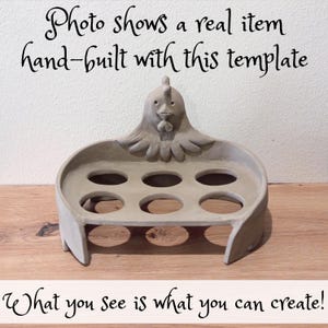 Op de afbeelding: Een lichtgrijze kleien eierhouder met een gebeeldhouwde kippenkop op het achterpaneel en zes ronde uitsparingen voor eieren. De tekst luidt: Photo shows a real item hand-built with this template. What you see is what you can create!