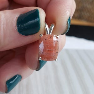 May include: A silver pendant with a square-shaped, peach-colored gemstone. The gemstone has a sparkly, iridescent finish.