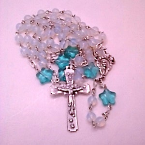 May include: A silver rosary with white and blue glass beads. The rosary features a silver crucifix and a silver charm.