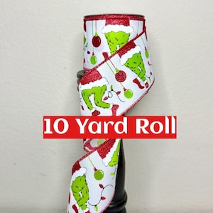 May include: A 10-yard roll of white ribbon with a festive Grinch-themed design. The ribbon features the Grinch's legs, Santa hat, and Christmas ornaments in green, red, and white. The edges are trimmed with red glitter.
