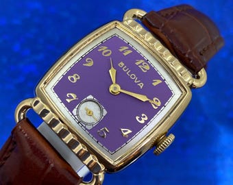 Könnte beinhalten: Eine goldfarbene Bulova Armbanduhr mit einem lila Zifferblatt und goldenen Zeigern. Die Uhr hat ein quadratisches Zifferblatt und ein braunes Lederarmband.