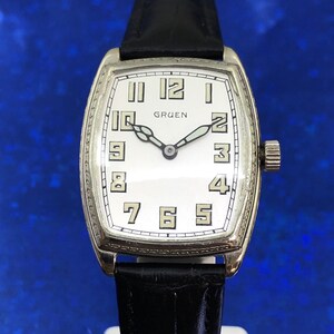 Pu&ograve; includere: Un orologio da polso Gruen argentato con quadrante bianco e lancette nere. L'orologio ha una cassa rettangolare e un cinturino in pelle nera.
