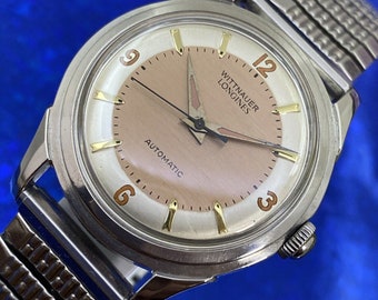 May include: A silver wristwatch with a white face and gold accents. The watch has a brown leather strap and says "Wittnauer Longines Automatic" on the face.
