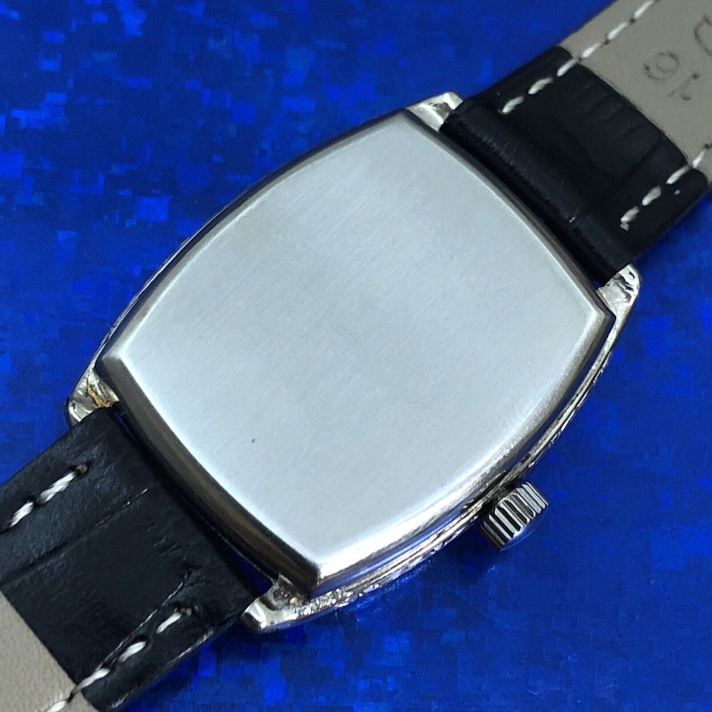 Pu&ograve; includere: Il retro di un orologio da polso argentato con un cinturino in pelle nera. L'orologio ha una finitura liscia e spazzolata e una piccola manopola sul lato.