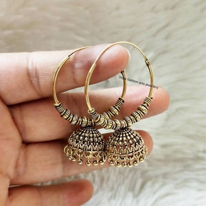 May include: Gold hoop earrings with a dangling jhumka design. The hoops are decorated with small beads and the jhumkas have intricate details.