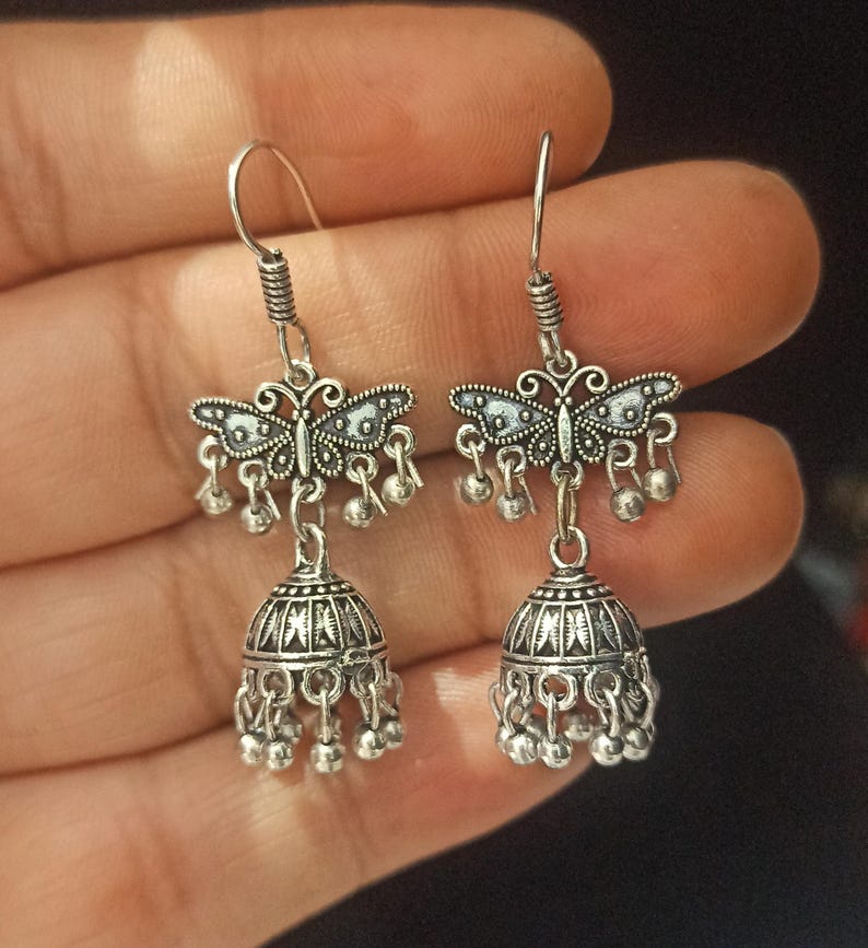 May include: A pair of silver earrings with a butterfly design and a bell-shaped dangle. The earrings have a silver hook closure.