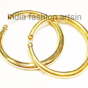May include: Two gold-colored metal bangles, one slightly larger than the other, are stacked on top of each other. The bangles are smooth and have a shiny finish.