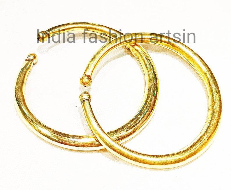 May include: Two gold-colored metal bangles, one slightly larger than the other, are stacked on top of each other. The bangles are smooth and have a shiny finish.