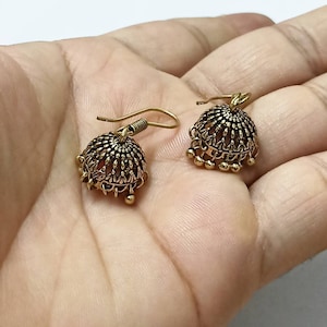 Puede incluir: Un par de pendientes colgantes de tono dorado con un diseño de filigrana y pequeñas cuentas redondas que cuelgan de la parte inferior.