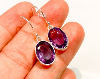 May include: A pair of silver dangle earrings with oval-shaped amethyst gemstones. The earrings have a simple design and are a beautiful shade of purple.
