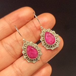 May include: A pair of silver dangle earrings with pink gemstone drops. The earrings feature a delicate, intricate design with a floral motif.