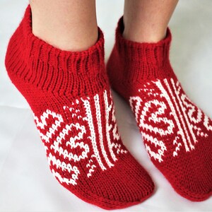 May include: Red knitted socks with a white geometric pattern. The socks are ankle-high and have a ribbed cuff.