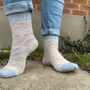 Puede incluir: Calcetines de punto con un patrón azul claro y beige, usados con vaqueros azules, con los bajos doblados en los tobillos. Los calcetines tienen un diseño texturizado y puntera y puño azul claro.