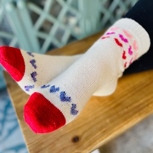 May include: White socks with red and purple hearts. The socks have a red toe and heel.