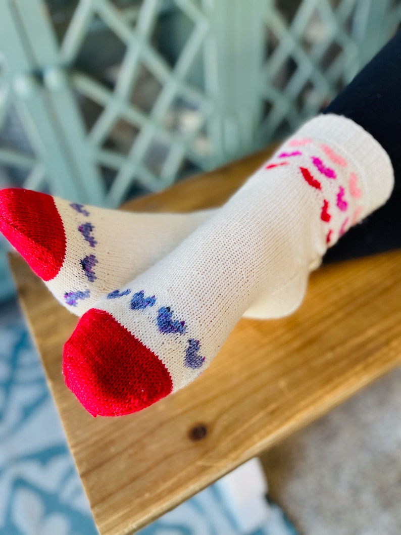 May include: White socks with red and purple hearts. The socks have a red toe and heel.